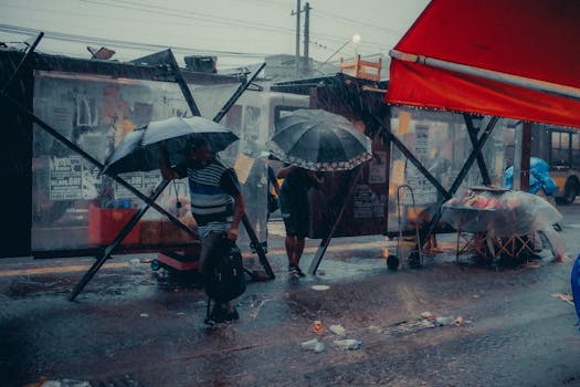 People with umbrellas at a city bus stop during heavy rain.