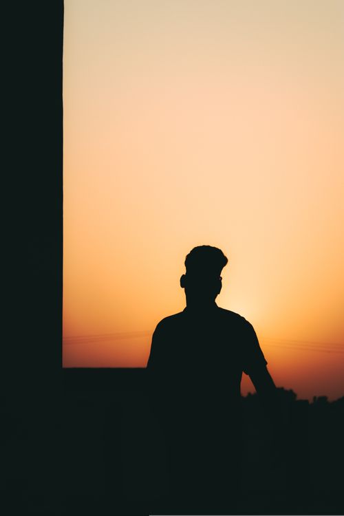 Free A silhouette of a man standing against a vibrant orange sky during sunset, creating a serene and moody atmosphere. Stock Photo