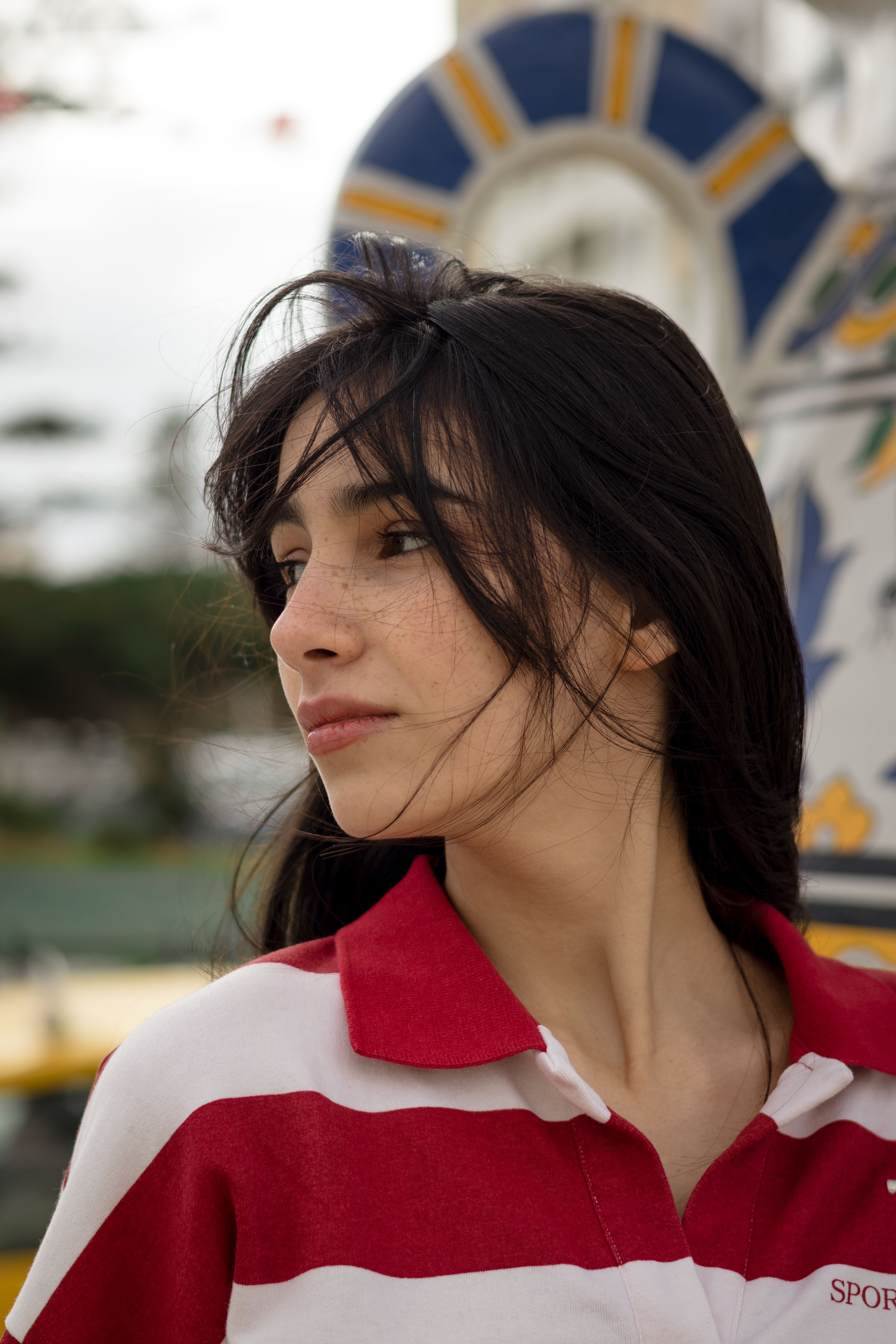 Portrait of a young woman with long brunette hair, wearing a red and white striped shirt at a fairground.