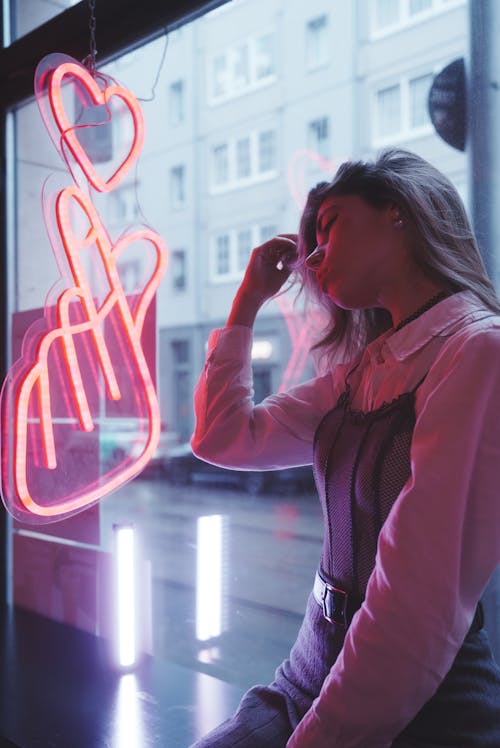 Young Woman Sitting by the Window with a Neon Sign