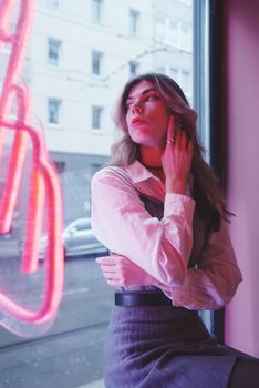 Portrait of a fashionable woman sitting by neon window in Berlin, showcasing urban style.