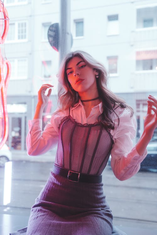 Young, Fashionable Woman Sitting by the Window with a Pink Neon Sign 