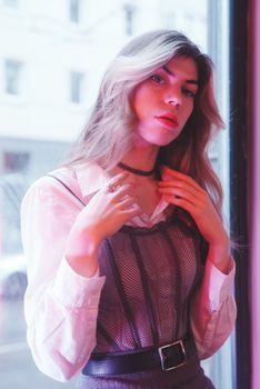 Fashionable young woman posing by a window with pink lighting in Berlin.