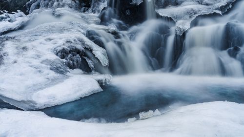 Free A serene winter scene of a frozen waterfall surrounded by ice and snow, captured in cool tones. Stock Photo