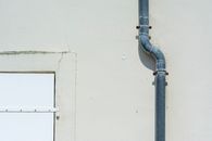 Close-up of a gray metal drainpipe attached to a plain exterior wall.