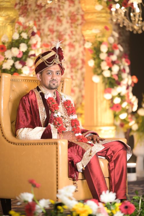 Free Indian groom in traditional red attire seated on an elaborate chair amidst floral decor. Stock Photo