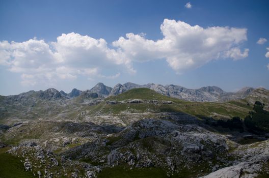 A tranquil mountain landscape with rocky hills under a clear blue sky and scattered clouds.