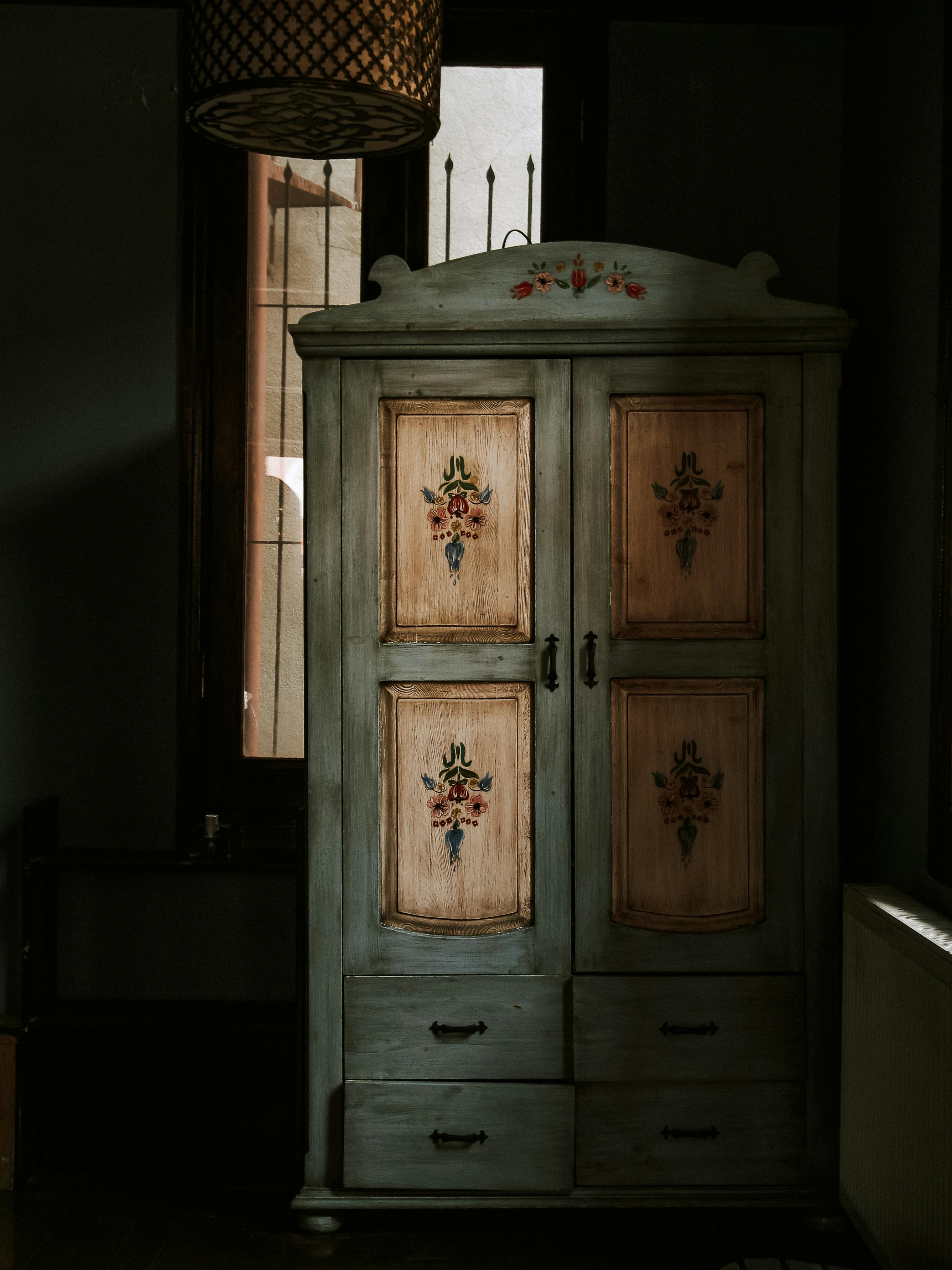 Classic wooden wardrobe with floral details in a dimly lit vintage room.