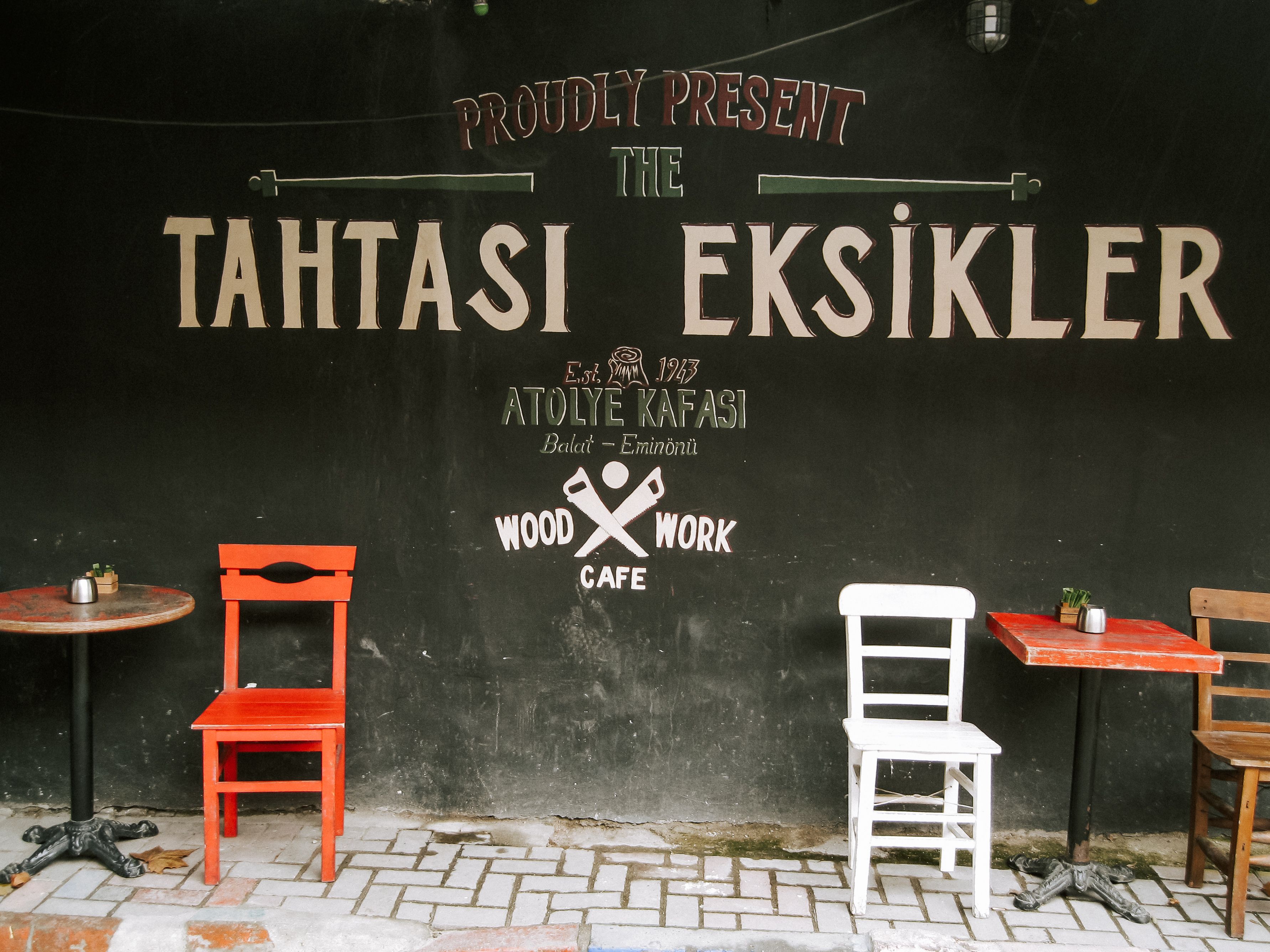 Three chairs against a rustic cafe wall in Tahtası Eksikler, Istanbul, creating a vibrant street scene.