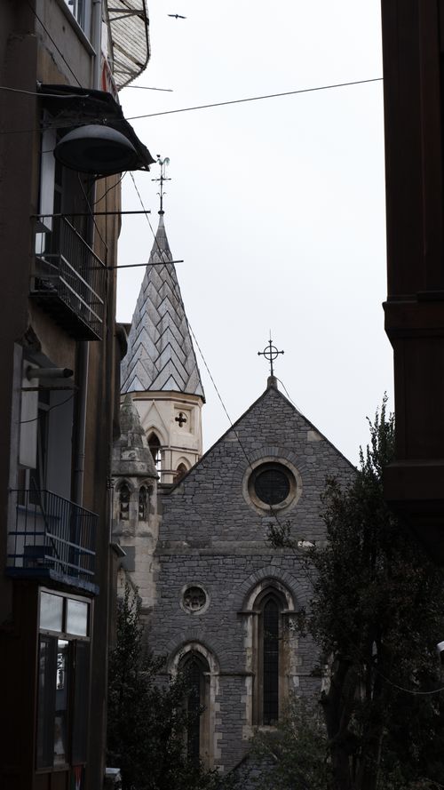 Free View of a historic stone church nestled between urban buildings, showcasing architectural contrast. Stock Photo