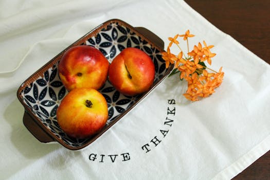 Top view of ripe nectarines in a patterned dish with flowers on a 'Give Thanks' cloth.