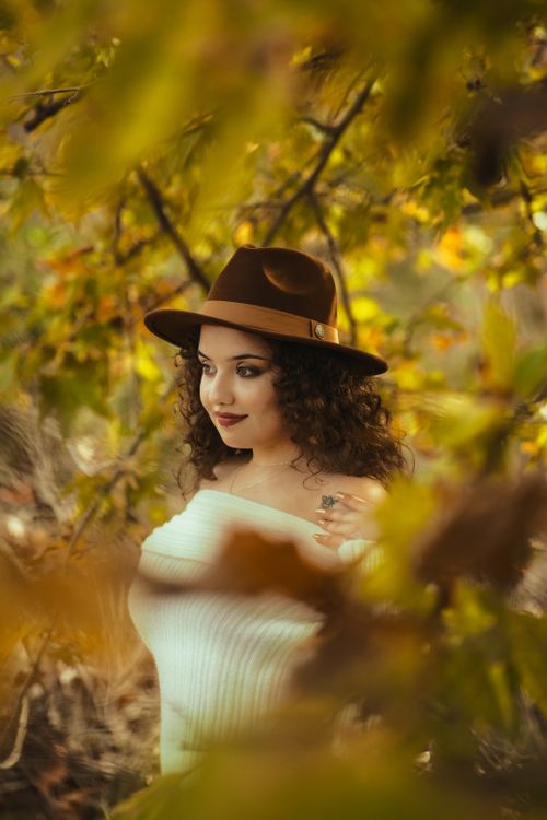 Free Portrait of a woman with curly hair and stylish hat in an autumn setting with vibrant leaves. Stock Photo