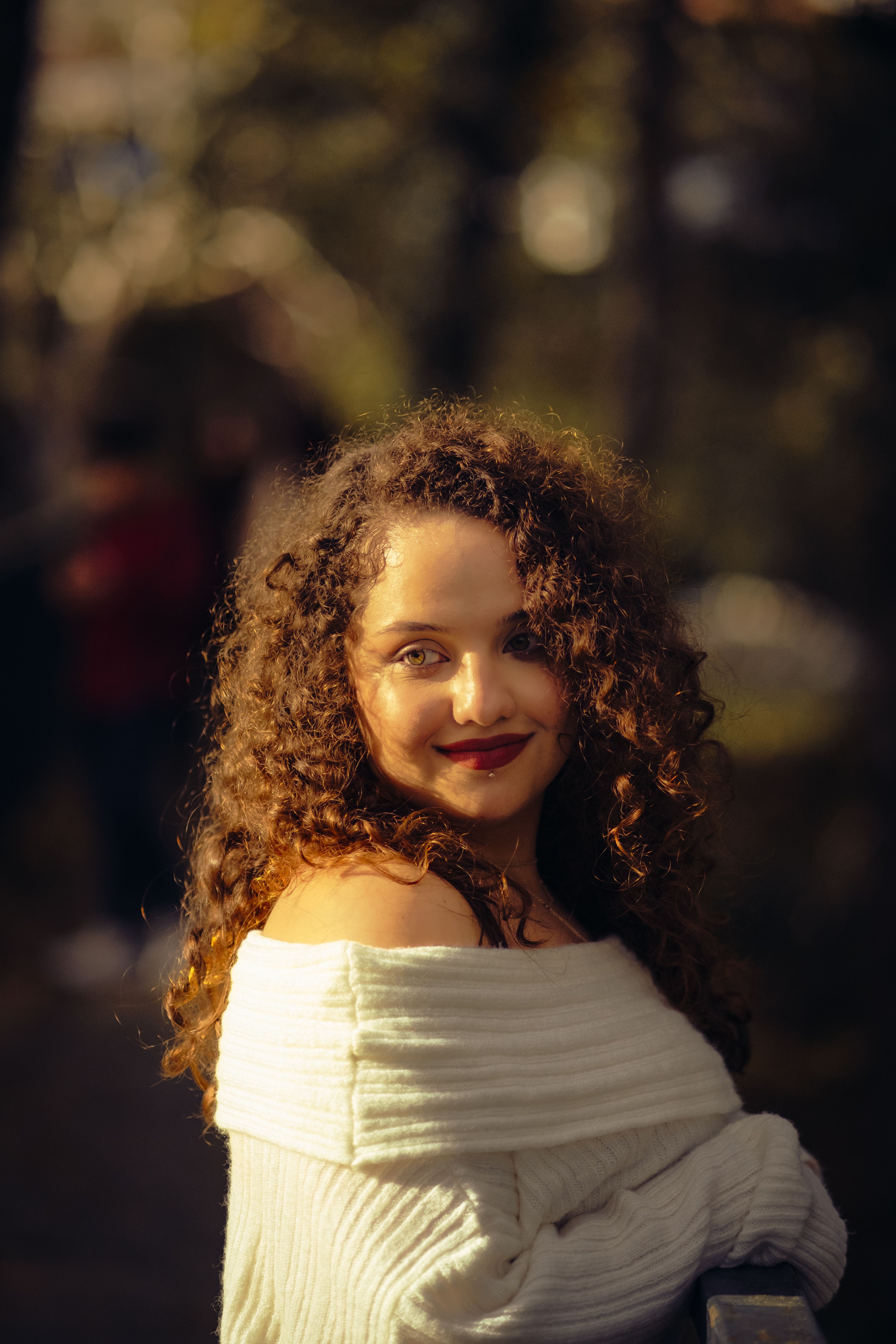 Beautiful woman with curly hair smiling outdoors in warm sunlight.