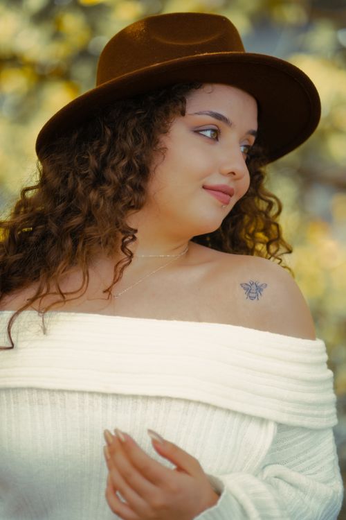 Free Portrait of a fashionable woman with curly hair and a tattoo, wearing a hat in natural light. Stock Photo