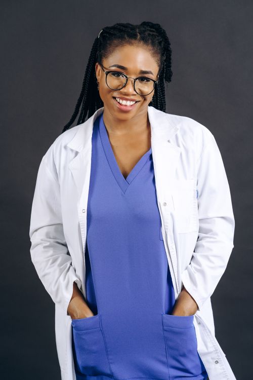 Free Smiling black woman doctor in scrubs standing confidently with hands in pockets. Stock Photo