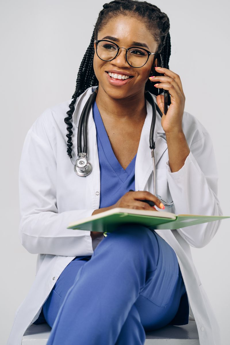 A Black woman doctor in scrubs reviews notes in a clinic, the setting where vaginal symptoms get an accurate diagnosis instead of a guess from a drugstore aisle.