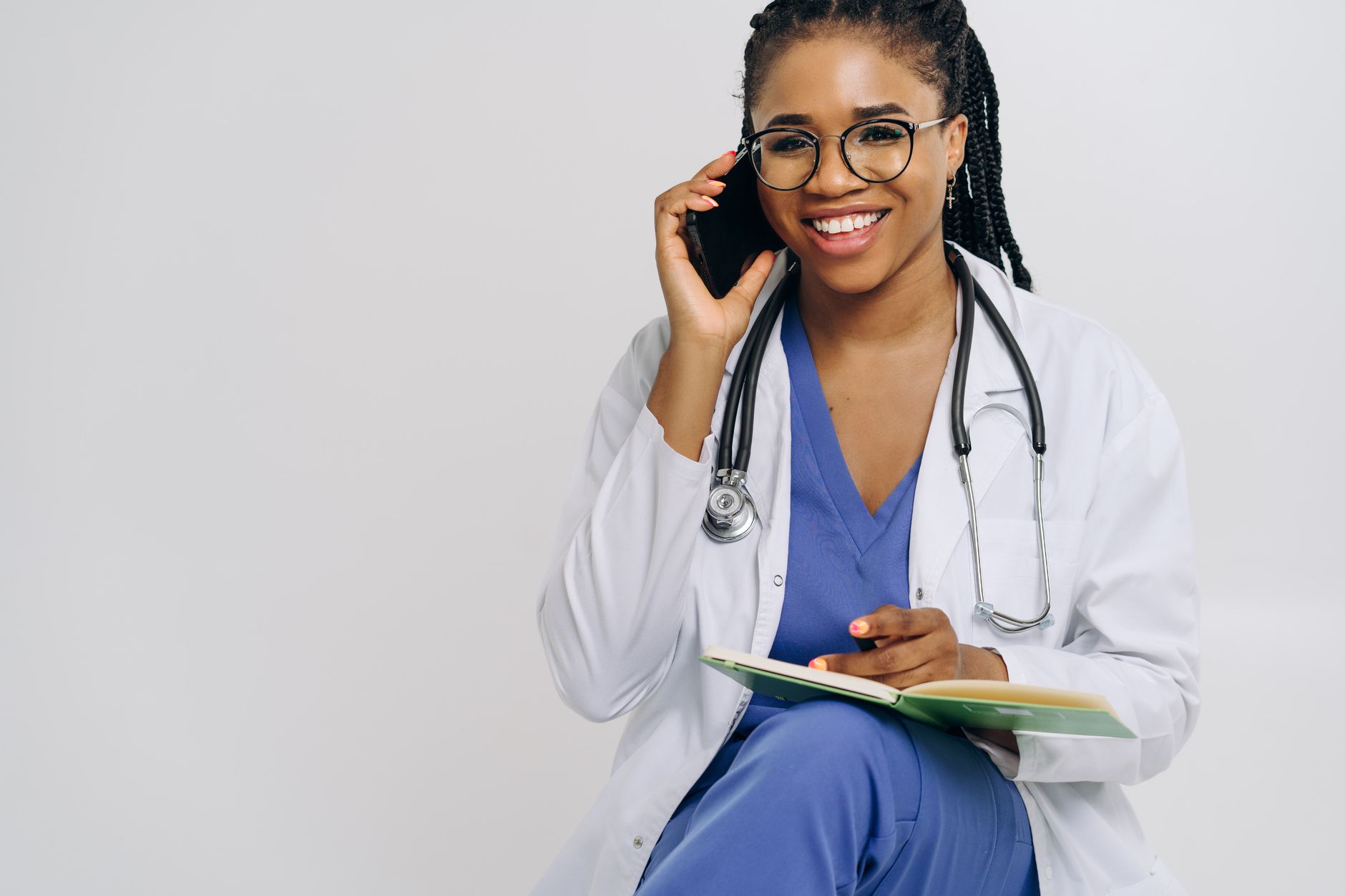 Cheerful female doctor in lab coat talking on smartphone and taking notes.