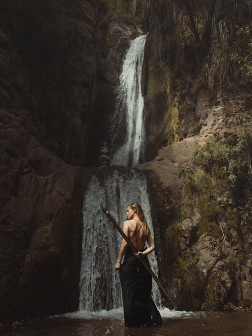 Model in a Black Backless Evening Dress Posing Under a Waterfall