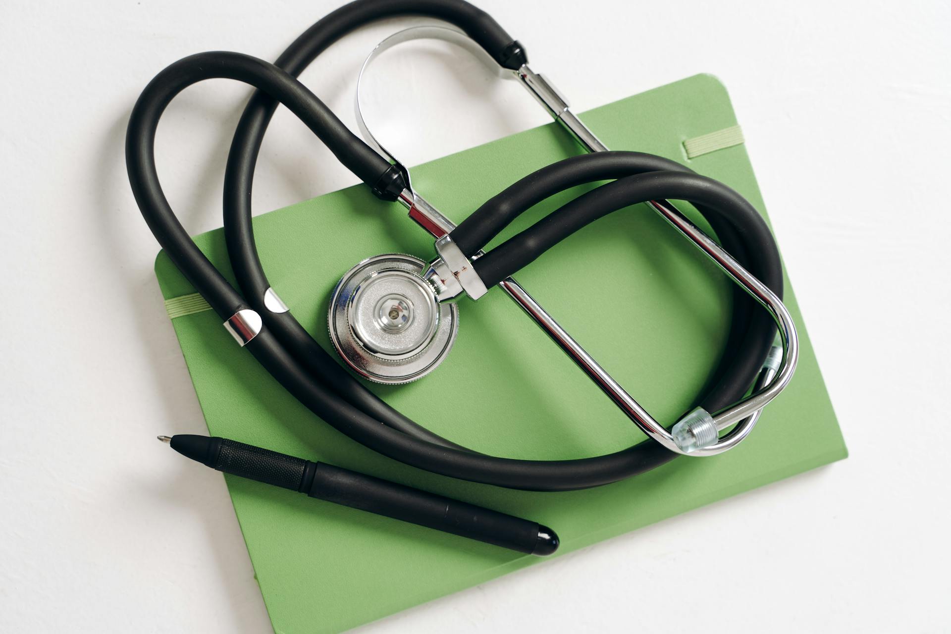 Top view of a stethoscope and pen on a green notepad, ideal for medical and educational themes.