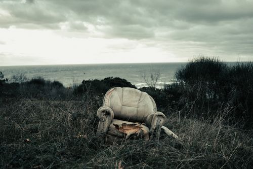 Free An abandoned armchair sits in a grassy field by the coast, under a moody sky. Stock Photo