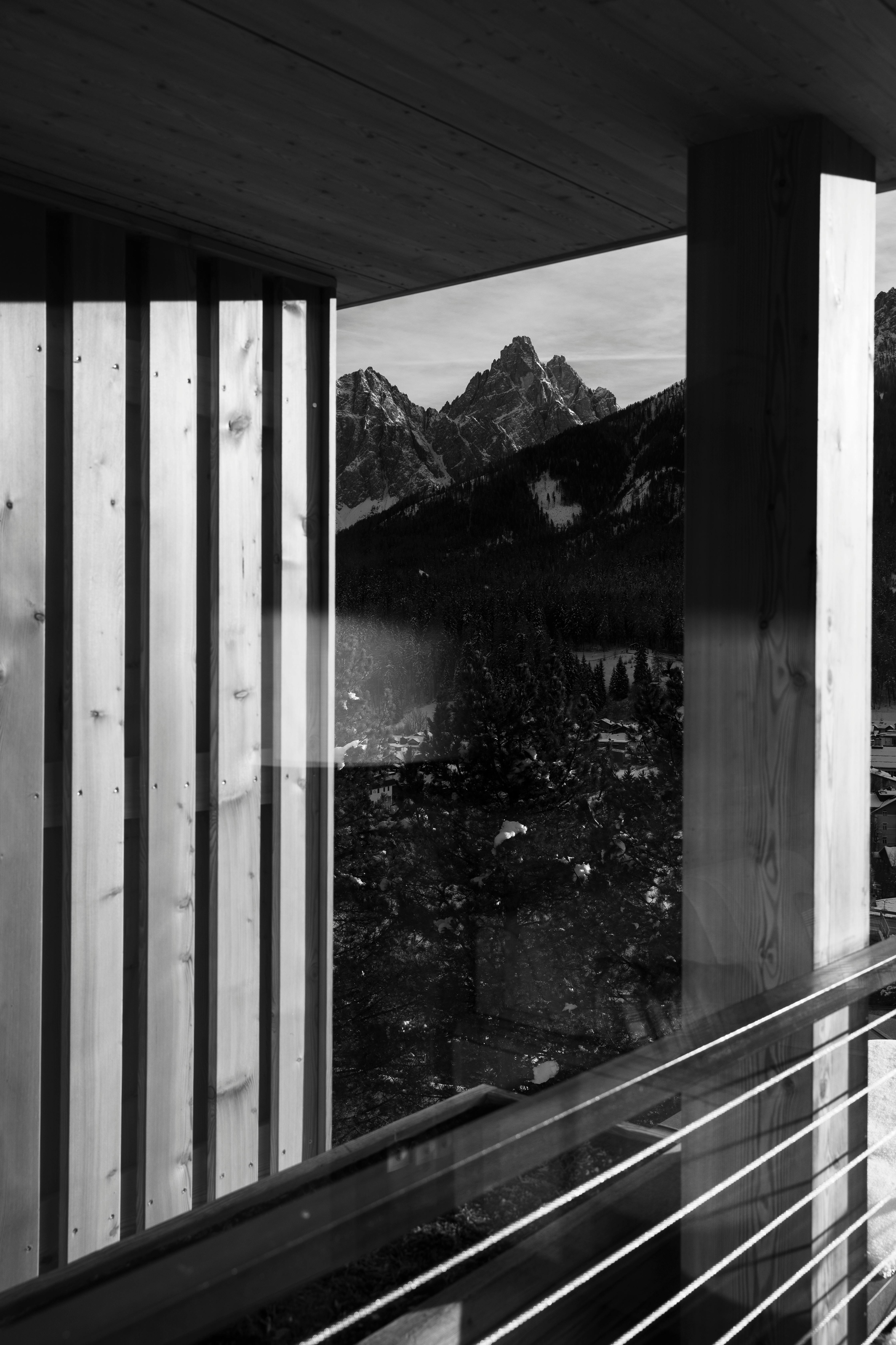 Serene black and white view of mountains from a wooden porch, capturing winter's essence.
