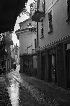Black and white shot of Bellagio's charming streets in the rain, with people under umbrellas.