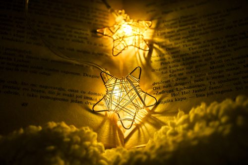 Free Close-up of glowing star-shaped string lights on book pages, creating a warm, cozy atmosphere. Stock Photo