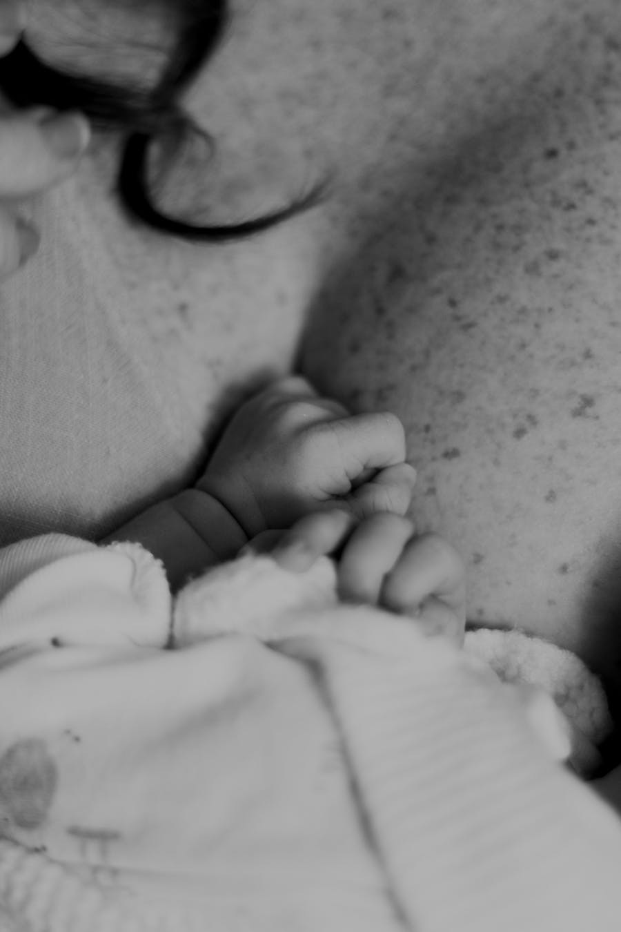 A newborn's tiny hands resting on a parent's chest, showing the scale and fragility of new life