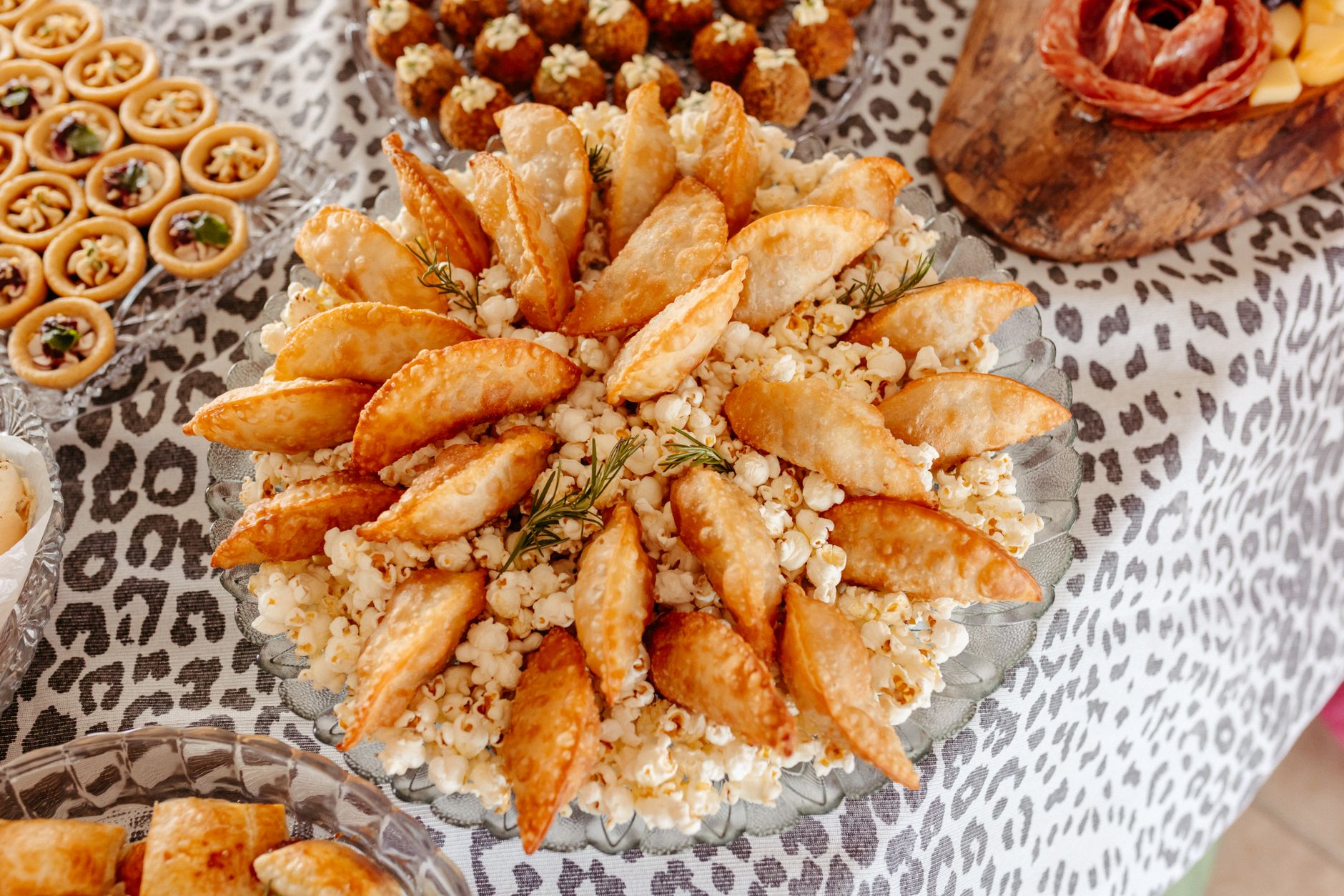 A variety of savory snacks including empanadas and popcorn on a leopard print tablecloth for a party setting.