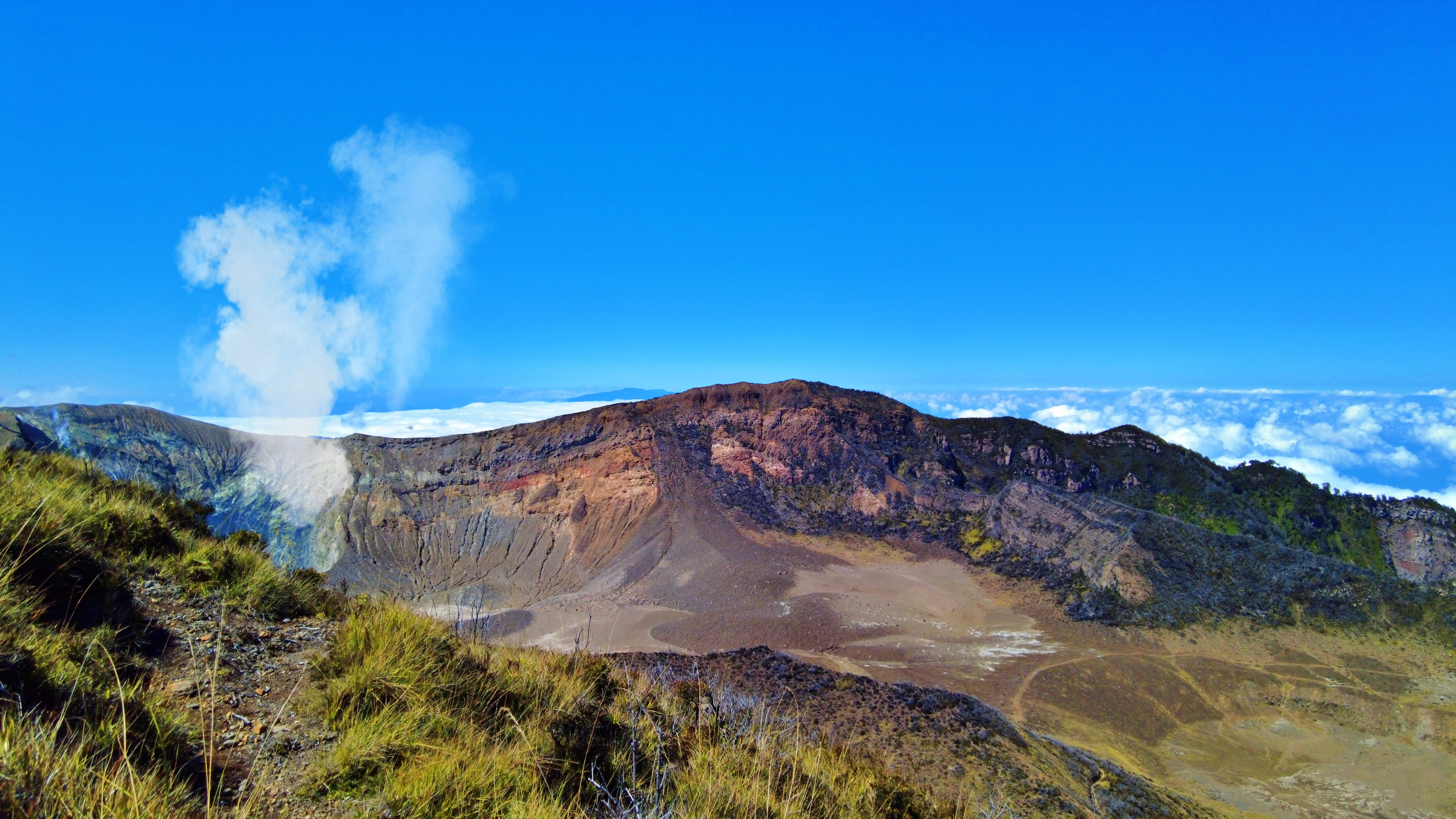 A breathtaking aerial view of a volcanic crater surrounded by a clear blue sky and fluffy clouds.
