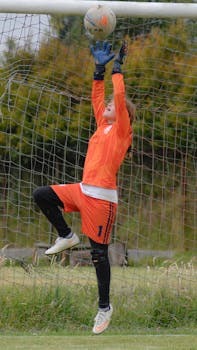 A young female goalkeeper in action, making a save during a soccer game.