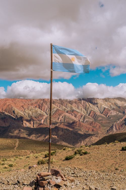 Free Argentinian flag waving against a stunning mountain backdrop under a bright sky. Stock Photo