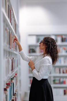 A woman in a modern Stuttgart library browsing books on shelves with a focused expression.