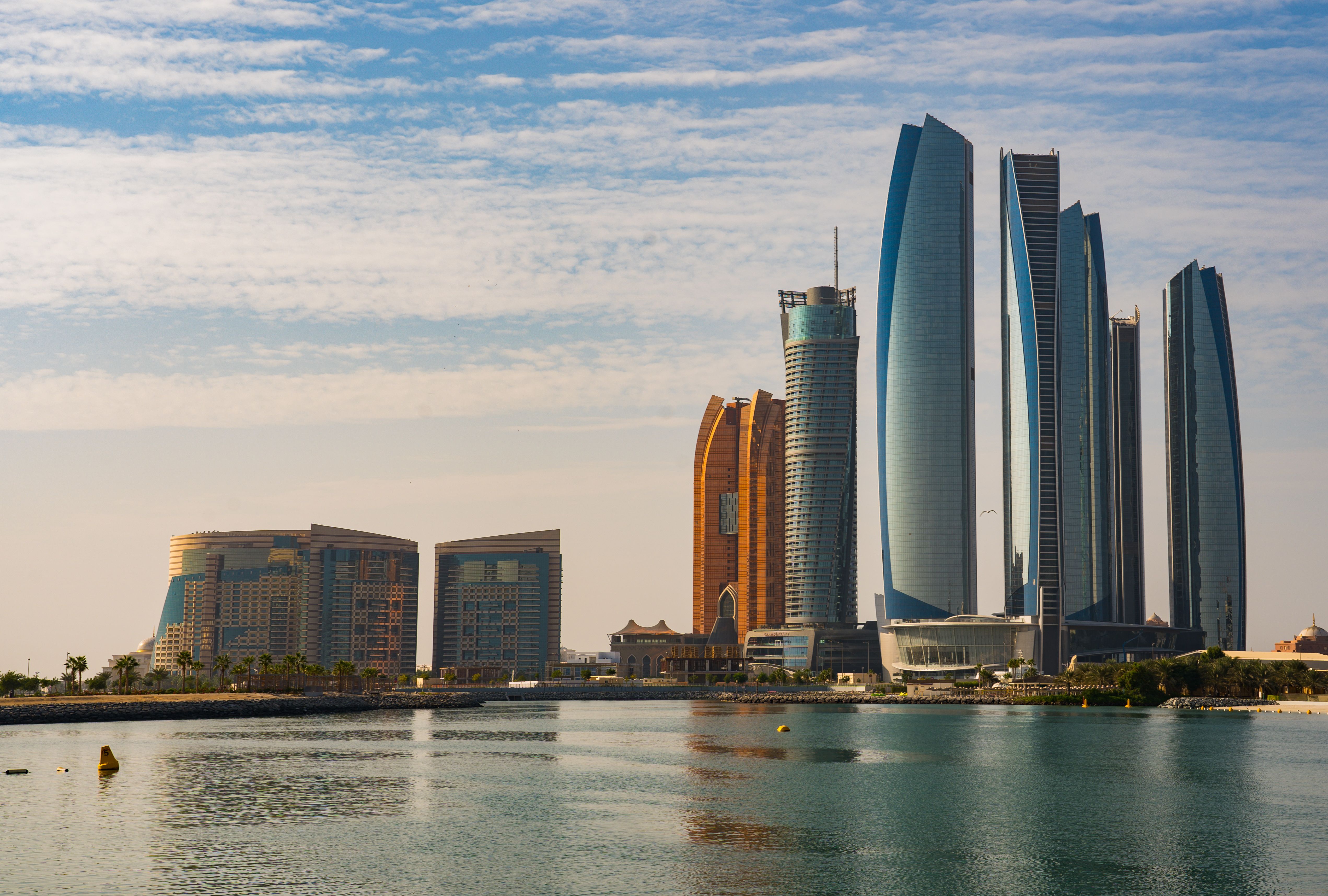 Daytime skyline near The Founder's Memorial in Abu Dhabi, United Arab Emirates, with waterfront towers and calm water.