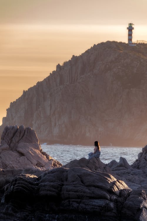 Woman Sitting on Rocks on Sea Coast