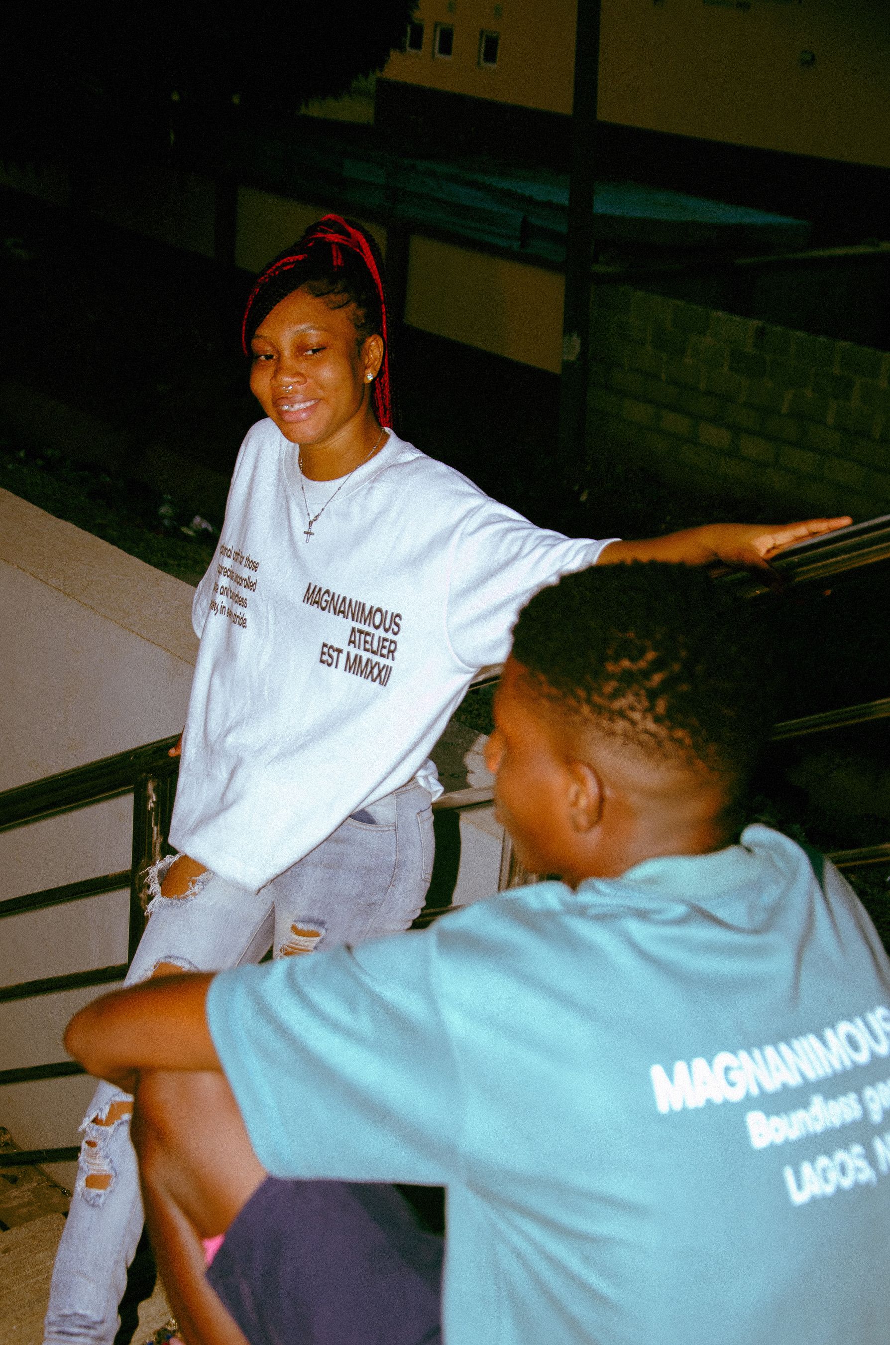 Two young adults smiling and sitting outdoors at night, conveying a relaxed and urban vibe.