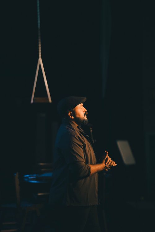Free Side profile of a man in an ivy cap during a dark night scene, clasping hands. Stock Photo