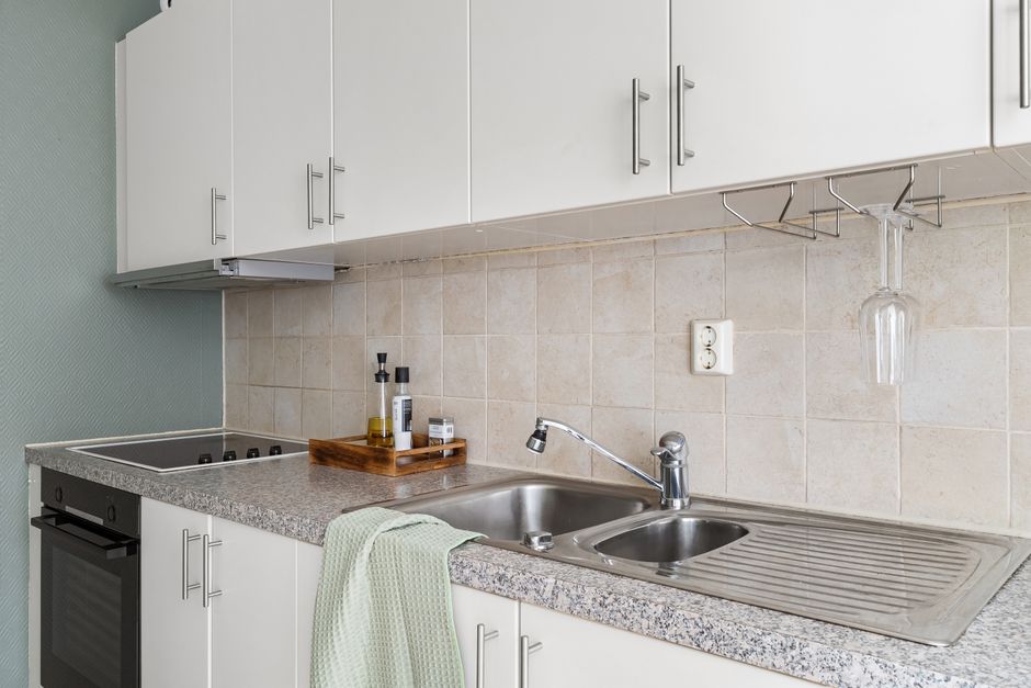 Jasna mała kuchnia w bloku z wielkiej płyty z białymi szafkami, blatem laminowanym i płytkami 60x60 cm na ścianie nad blatem