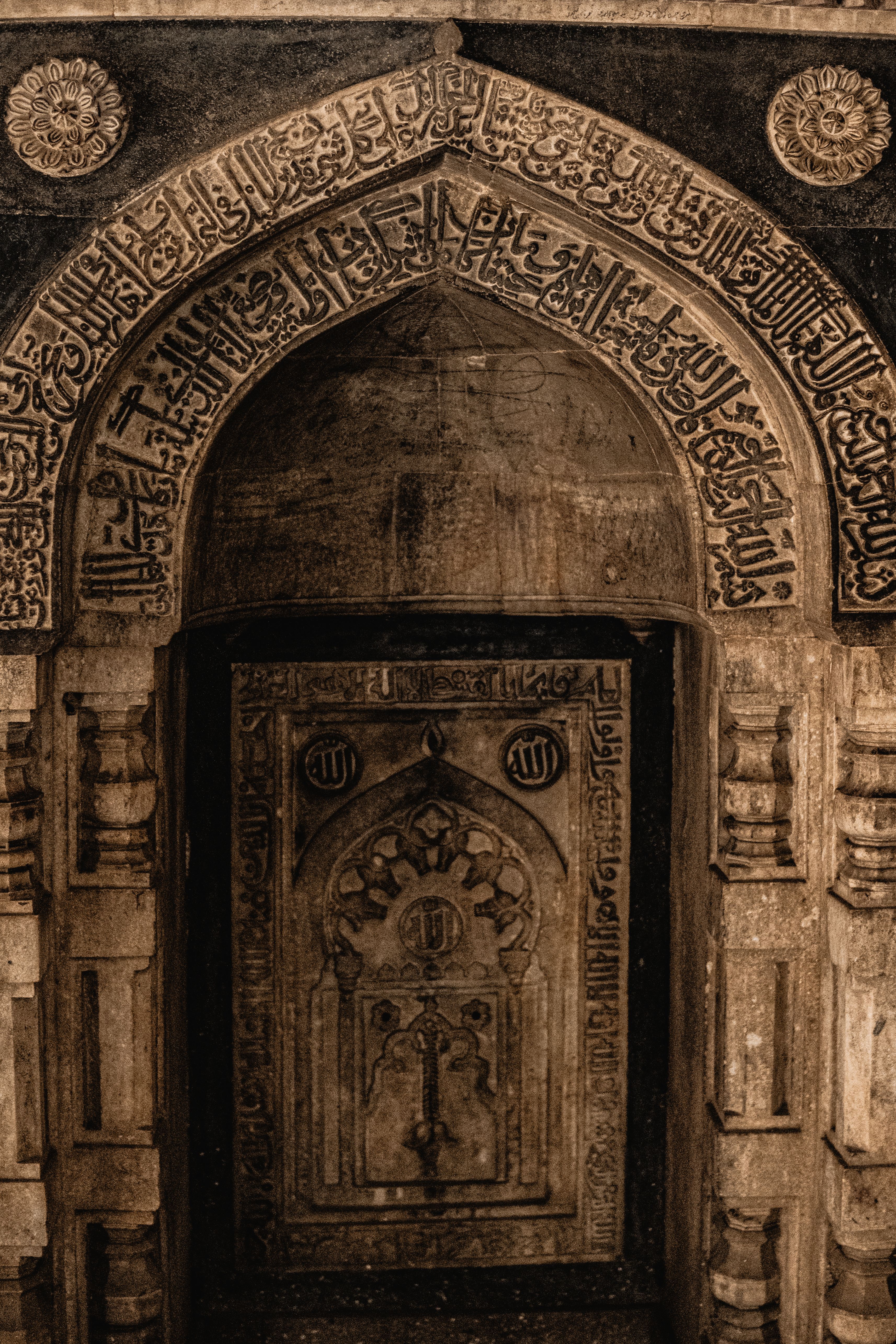Detailed view of an ornate stone arch with Arabic script in Isa Khan's tomb, Delhi.