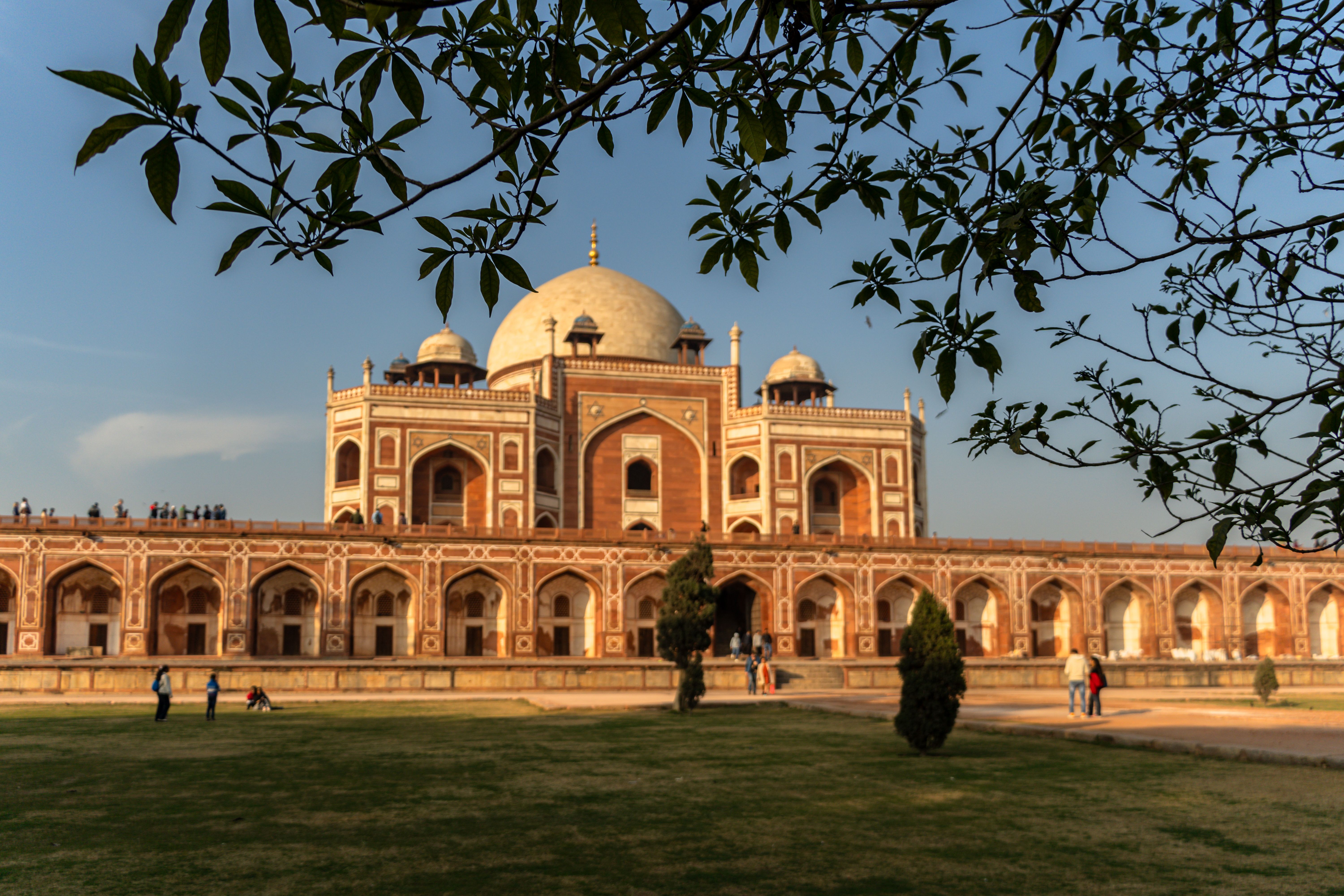 Domes of a Mughal tomb silhouetted against an orange Delhi sky at dusk