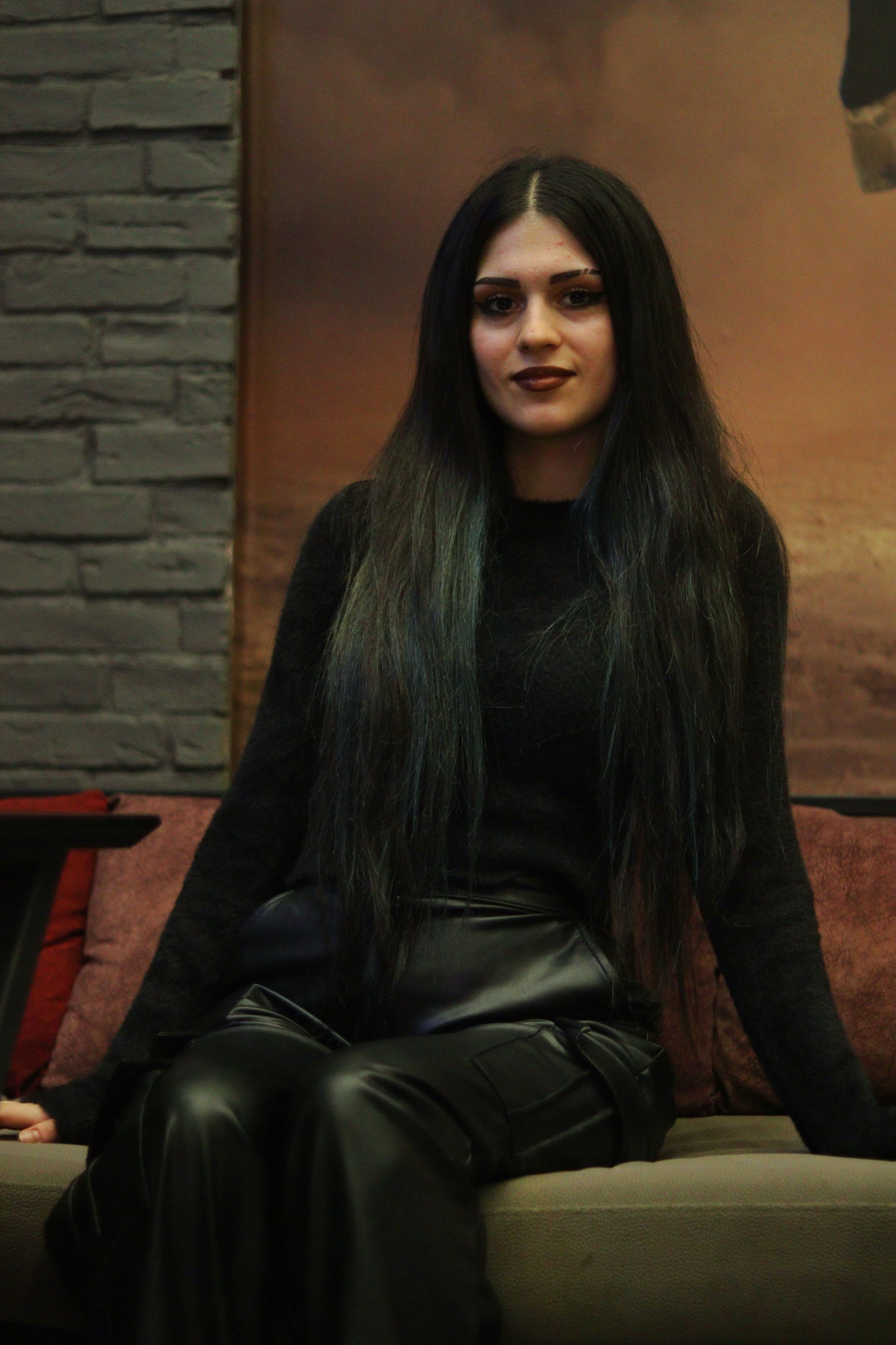 Stylish woman in black attire sitting elegantly on a sofa, showcasing glamour and sophistication.