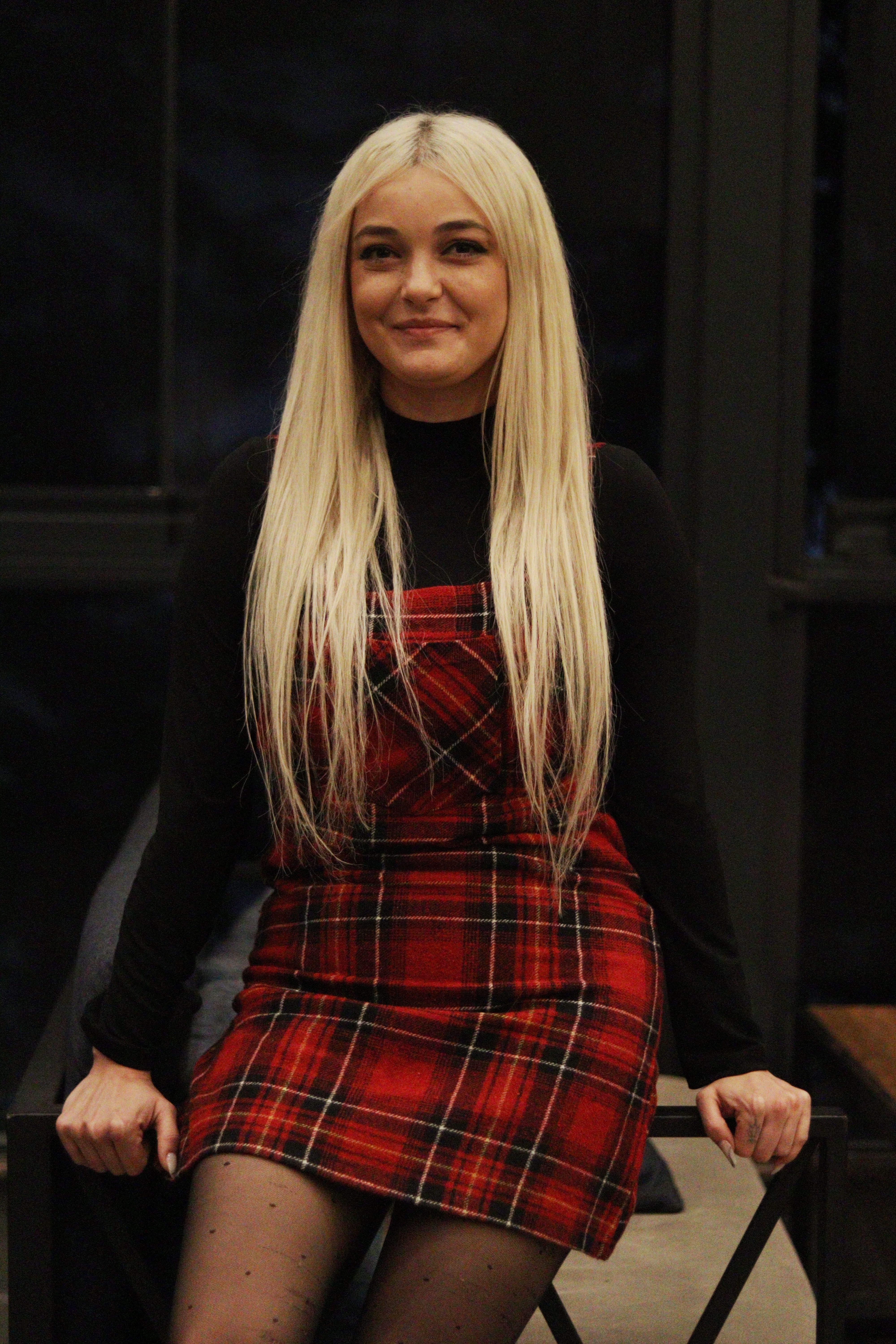 Fashion portrait of a woman with platinum blonde hair in a red tartan dress sitting indoors.