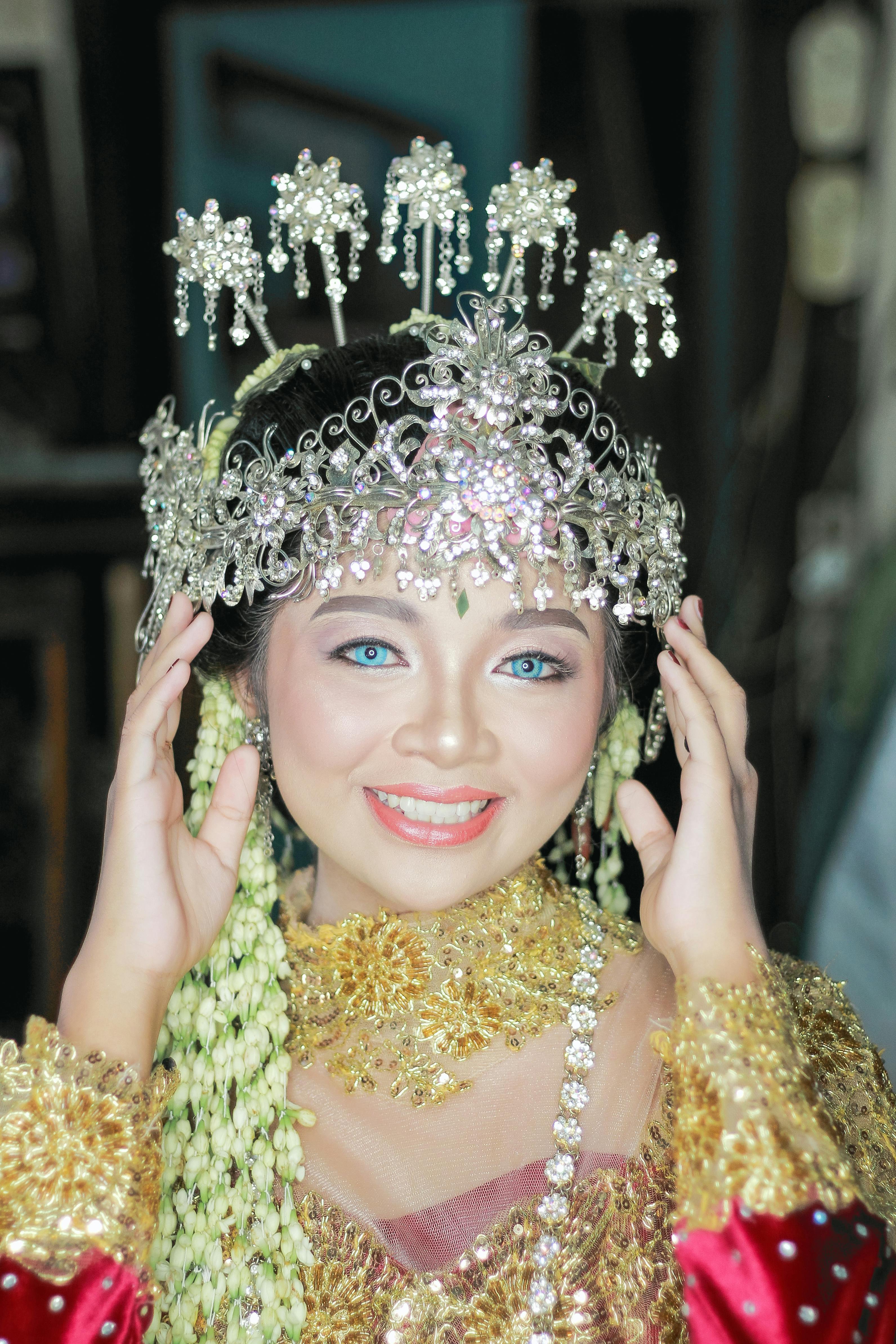 Portrait of a smiling Sundanese bride in traditional attire wearing intricate jewelry and crown.