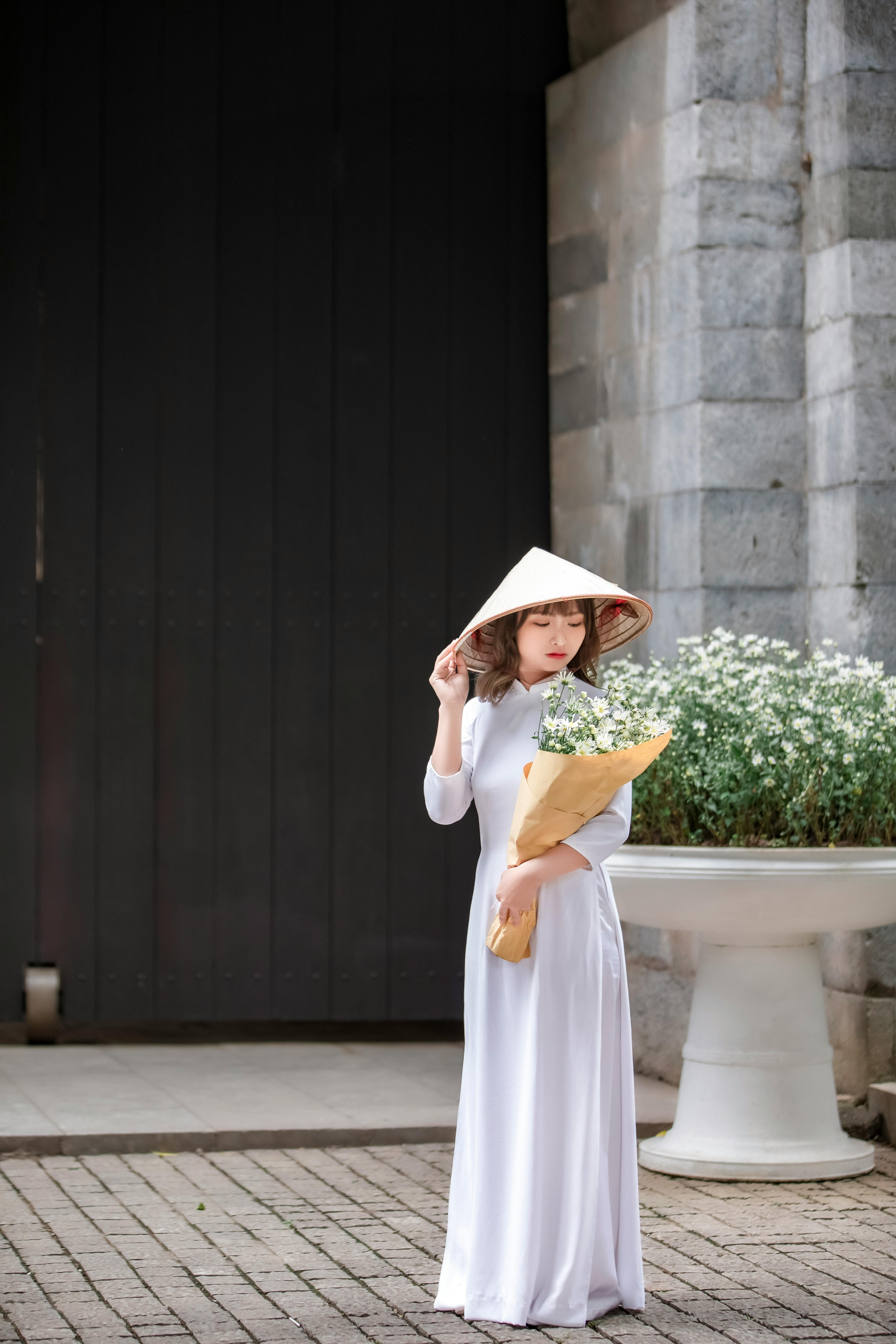 A woman in traditional attire holding a bouquet stands by an architectural structure.