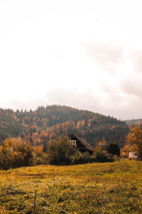 Free Rustic farmhouse amidst colorful autumn trees and rolling hills under cloudy skies. Stock Photo