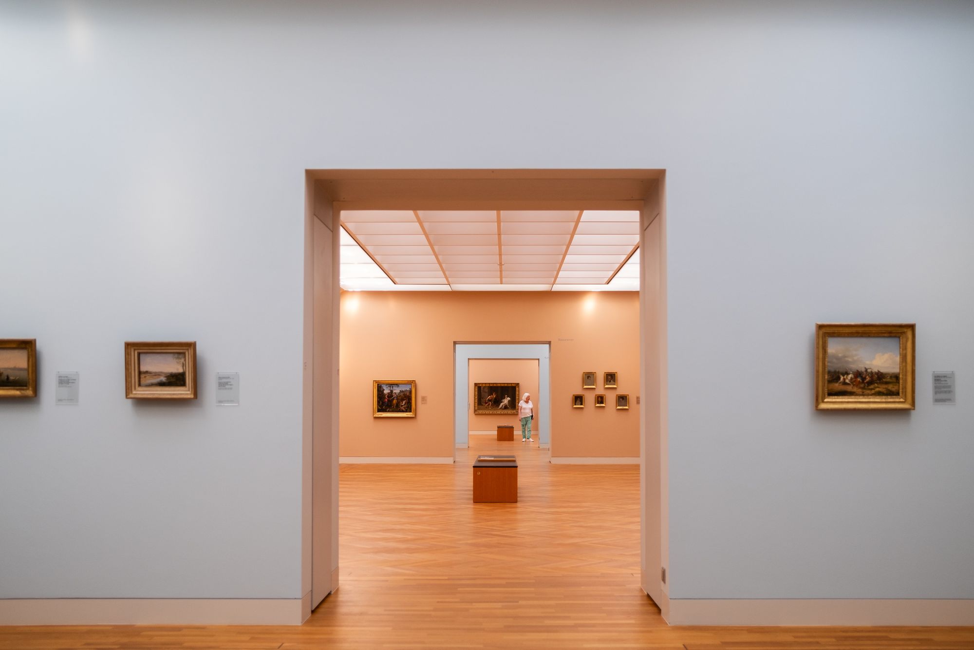 White-walled gallery rooms with framed paintings and wooden floors