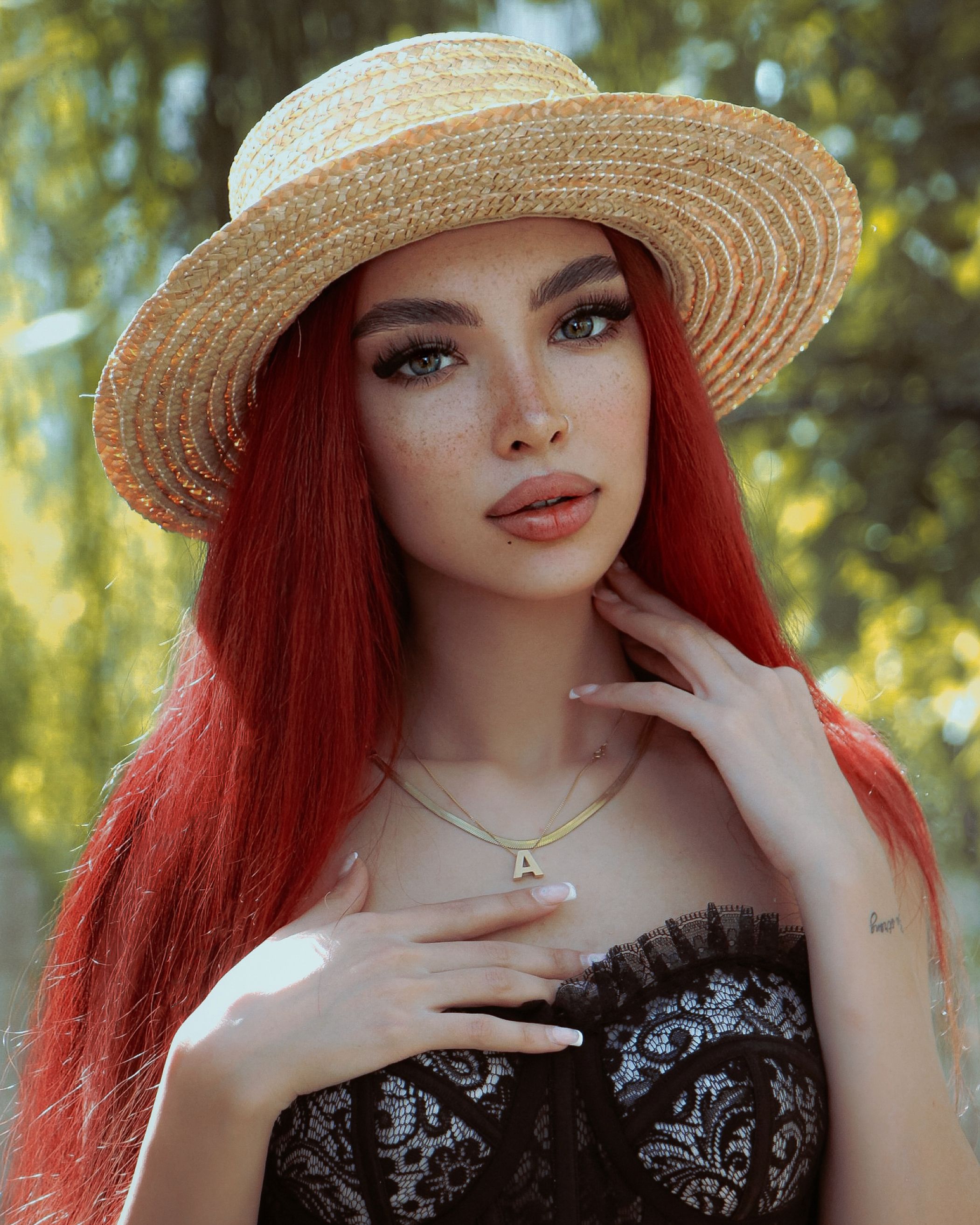 Elegant woman with vibrant red hair wearing a straw hat standing outdoors in sunlight.