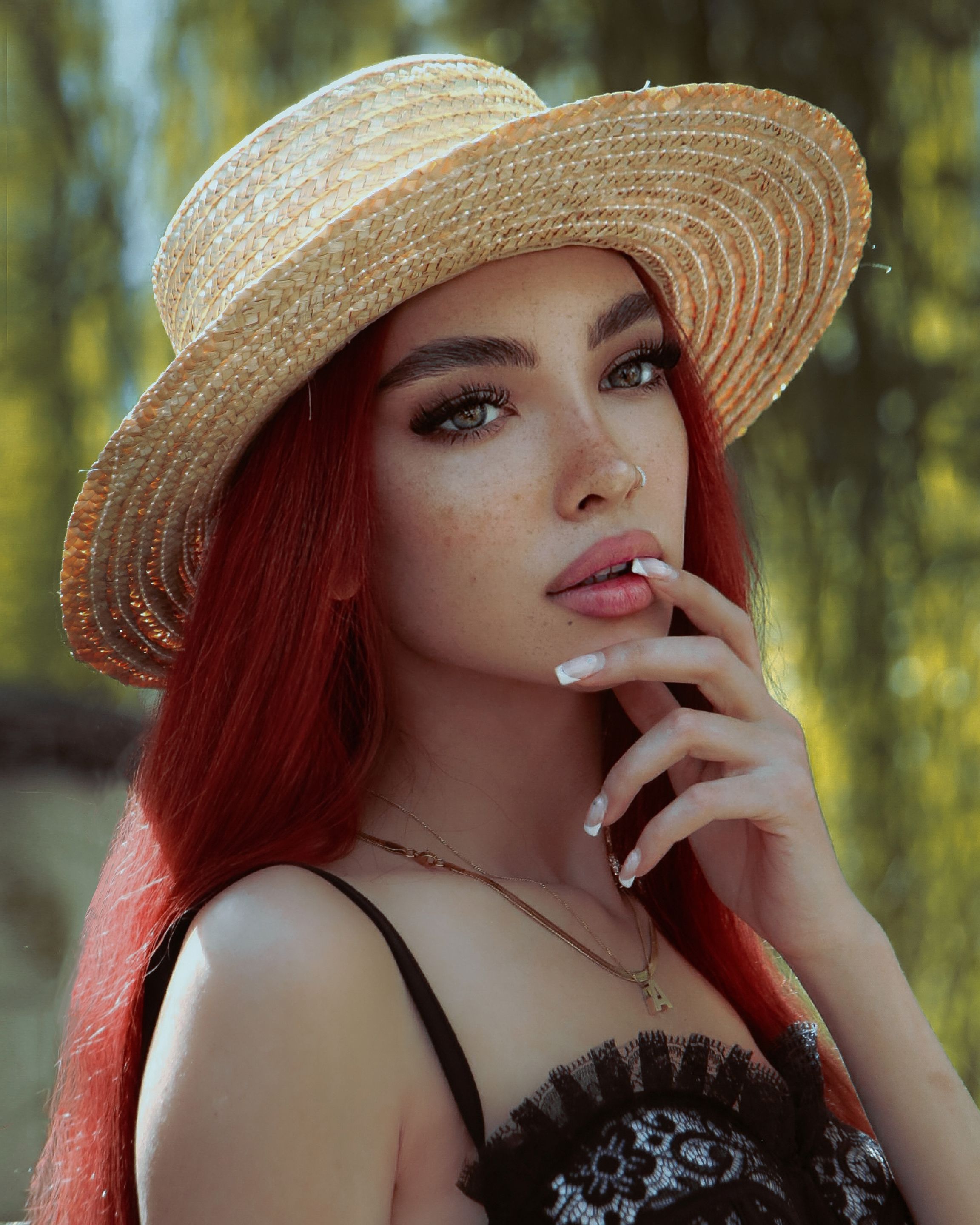 Stylish young woman with red hair wearing a straw hat in an outdoor setting. Captivating gaze and fashion-forward look.