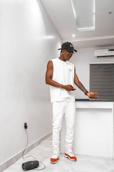 Young man in white outfit standing in modern apartment, showcasing casual style.
