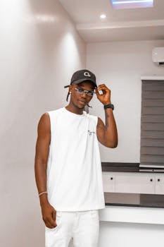 Fashionable young man in a white tank top and cap posing confidently indoors.